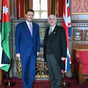 The Speaker of the House of Commons and the  Speaker of Jordan standing side by side in front of an ornate fireplace. The flags of Jordan and the United  Kingdom are at their sides.