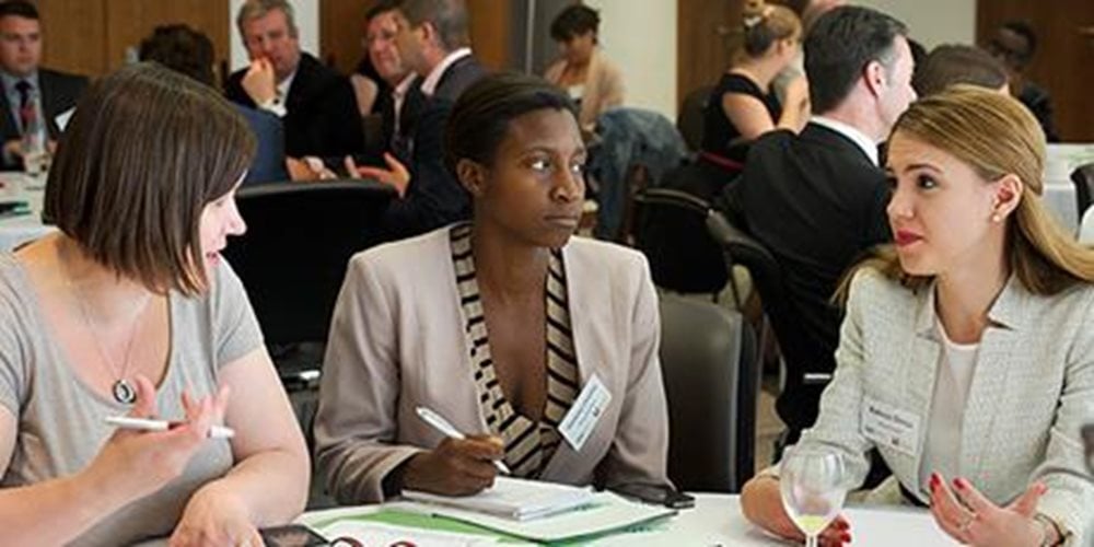 Three people sitting at a table at a conference, in conversation.