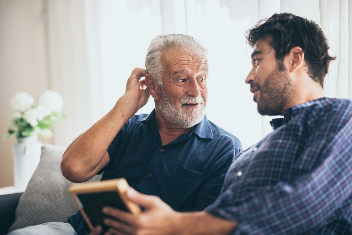 A man sits on a sofa speaking to his older father