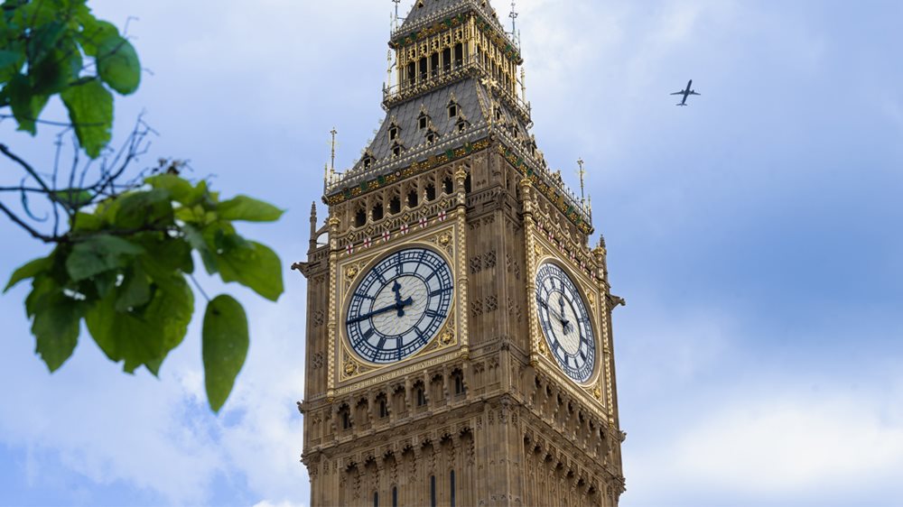 Elizabeth Tower with blue sky  behind and greenery in the foreground. A plane is flying overhead in the distance