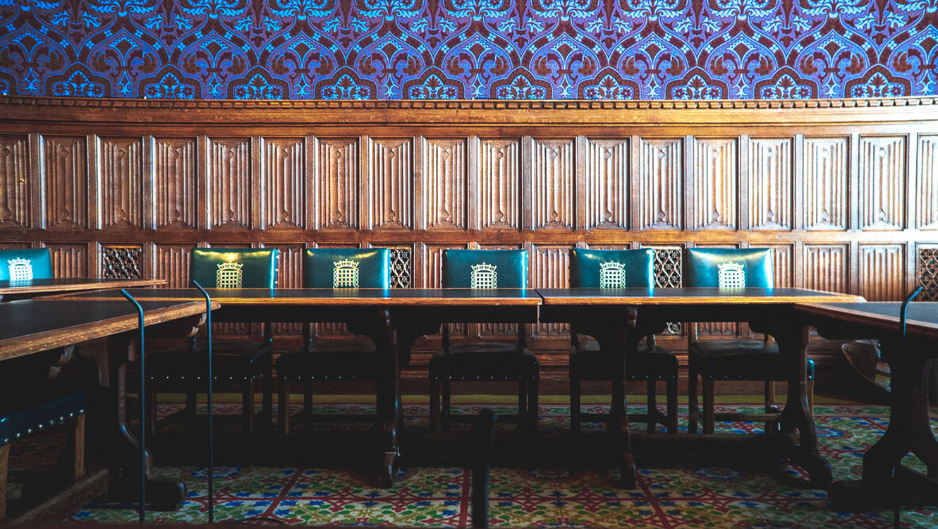 A wood pannelled room with decorative purlpe wall paper above the panelling. Five green leather chairs are behind a wooden table.