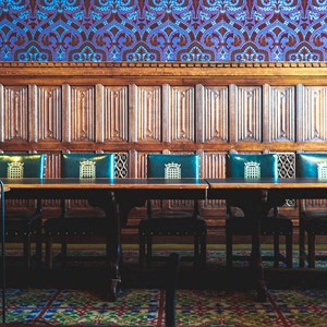 A wood pannelled room with decorative purlpe wall paper above the panelling. Five green leather chairs are behind a wooden table.