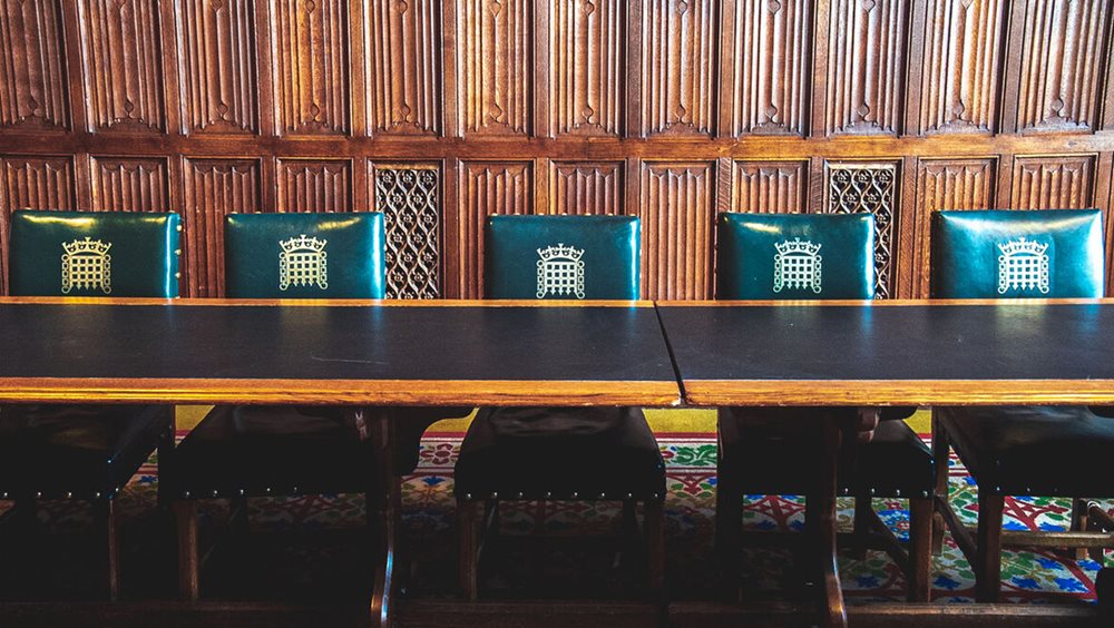 A wood panelled room with five green leather chairs behind a wooden table. There is a gold portcullis on the back of the chairs.