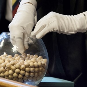 Bowl containg numbered balls. A gloved hands is selecting a ball from the ball