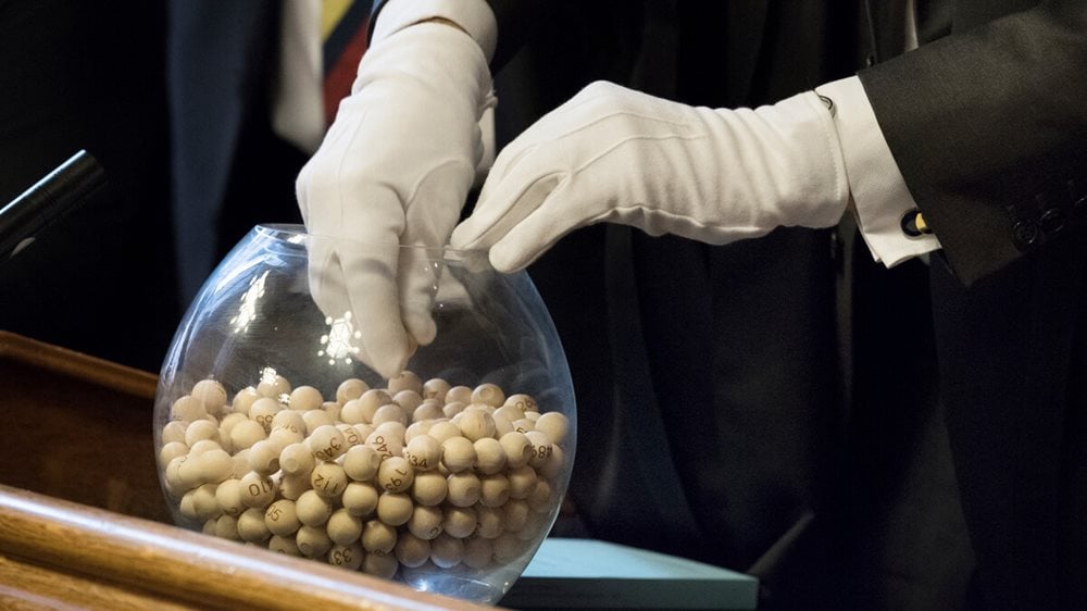 Bowl containg numbered balls. A gloved hands is selecting a ball from the ball